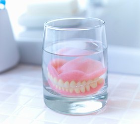Dentures in glass of clear fluid on white tiled surface