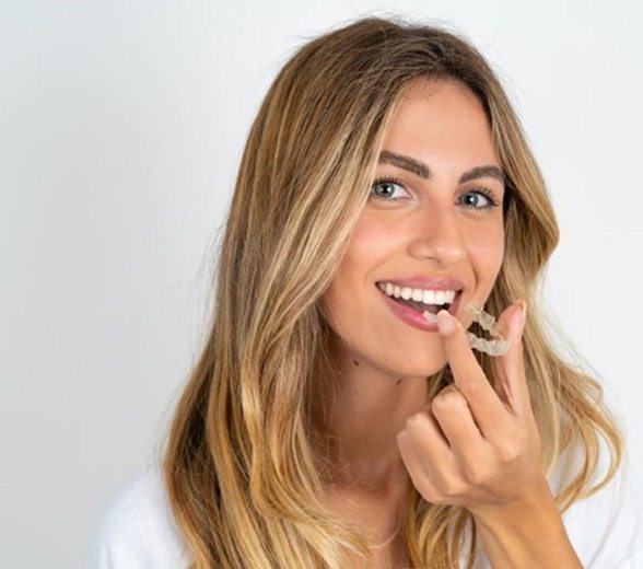 Smiling woman holding clear aligner near her mouth