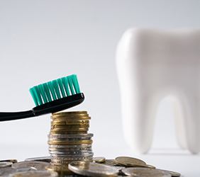 Dental crown model next to toothbrush on top of coin stack