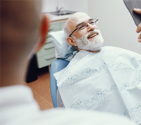 Man smiling at a mirror while sitting in dental chair