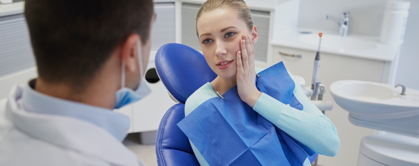 Woman in dental chair holding cheek in pain