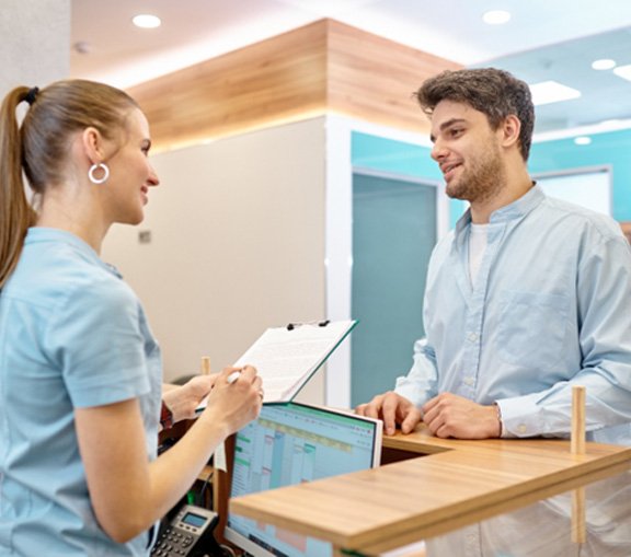 Man smiling while talking to dental receptionist