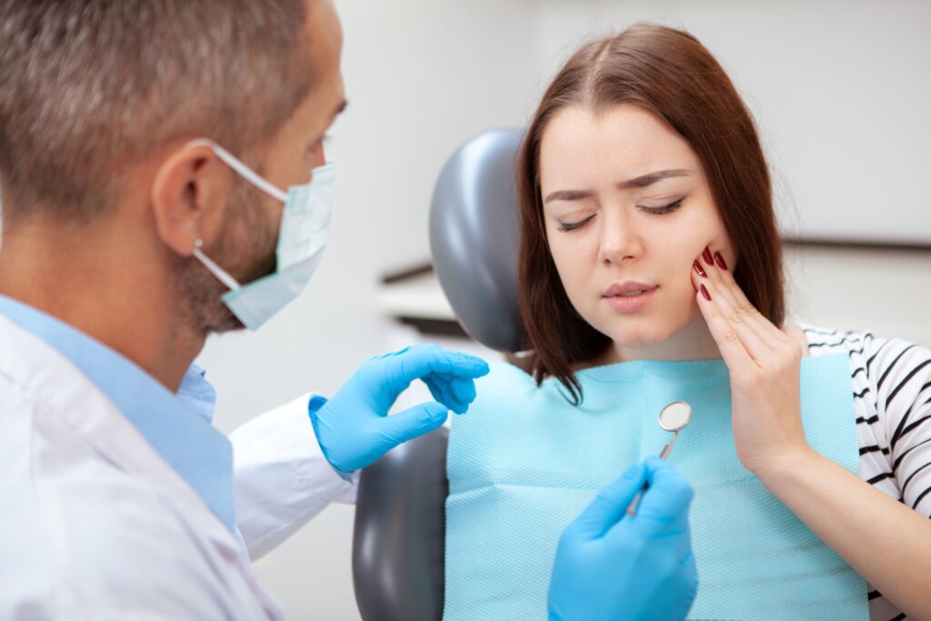 Woman with eyes closed in dental chair holding hand to face in pain